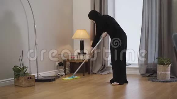 年轻的穆斯林女士清洁地板的肖像穿黑色头巾的年轻女士用拖把做家务东方文化视频的预览图