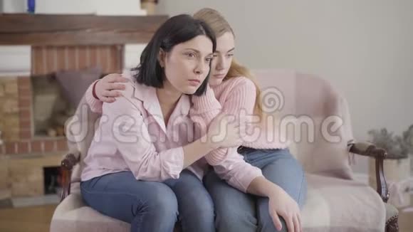 沮丧的白种人母女坐在家里的沙发上少女抱着妈妈成年女子抱着头视频的预览图