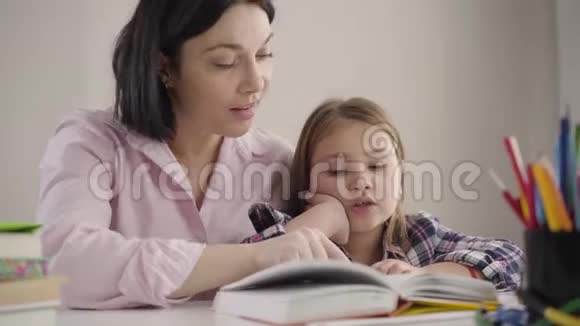 在家和妈妈一起看可爱的白种人女孩的书快乐的女学生和父母一起做作业母亲视频的预览图