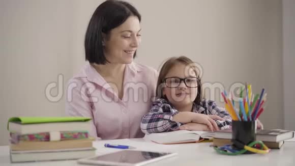 快乐的白种人女孩戴着眼镜和深色的成年女人看着相机和微笑的肖像友好的母亲视频的预览图