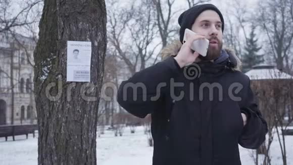 一个长着胡子的白人年轻人在打电话看着挂在树上的失踪人口广告神经病的家伙视频的预览图