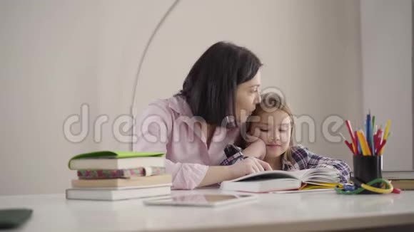 幸福的白种人母亲为女儿读书并亲吻她的头的肖像积极的女生做作业视频的预览图