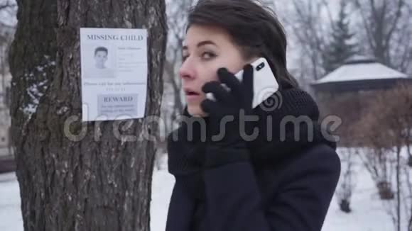 兴奋的白种人年轻女子打电话回顾挂在树上的失踪儿童广告的画像视频的预览图