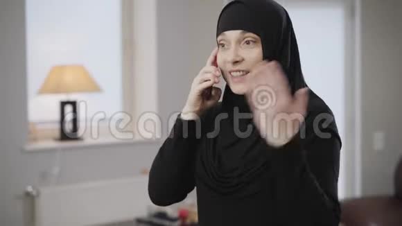 年轻的现代穆斯林妇女戴着头巾在智能手机上交谈并在情感上做手势的肖像东方女士视频的预览图