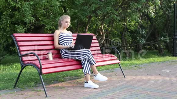 年轻女孩坐在公园长椅上时使用笔记本电脑视频的预览图