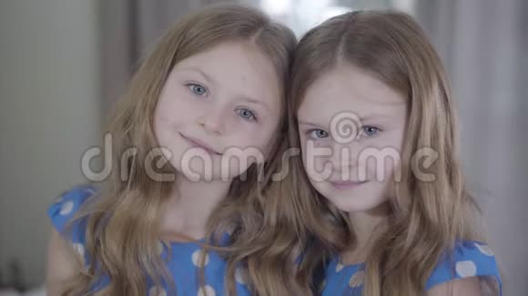 美丽的双胞胎姐妹在室内摆姿势的肖像冷静的孩子看着相机微笑着两个快乐女孩视频的预览图