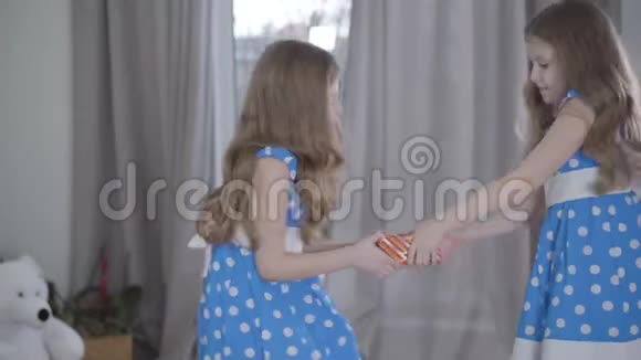 侧视两个小女孩争着要礼物穿着优雅蓝色连衣裙的布鲁内特双胞胎抱着礼物视频的预览图