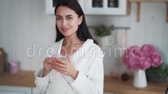 身着白色浴袍的年轻女子早晨在厨房喝茶的肖像视频的预览图