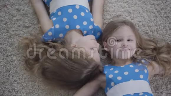 两个漂亮的高加索双胞胎姐妹躺在柔软的地毯上微笑的俯视图摄像机围绕着可爱的面孔移动视频的预览图
