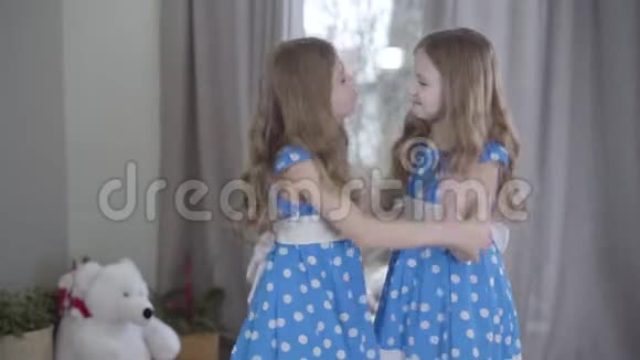 两个相同的姐妹在家玩得开心快乐的白种人双胞胎穿着蓝色点缀的裙子在室内跳舞视频的预览图