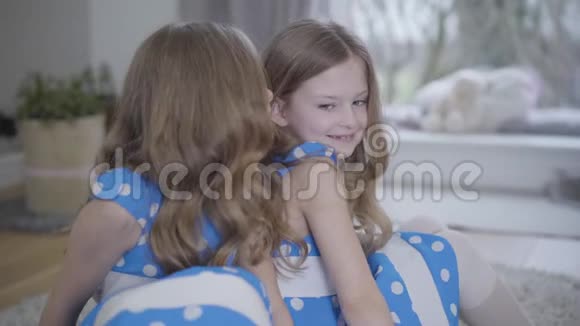 可爱的白种人黑发女孩穿着蓝色点缀的裙子微笑着听双胞胎妹妹在她耳边低语快乐视频的预览图