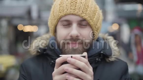 在街上喝热咖啡的冰冻白种人的特写镜头戴着黄色帽子的快乐男人视频的预览图