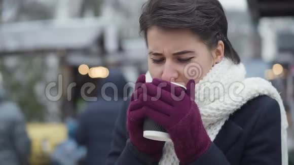 穿着白色围巾在户外喝咖啡的漂亮白种人女人的特写镜头棕色眼睛的冻僵的少女视频的预览图