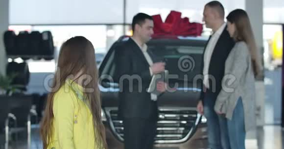开朗的小白种人女孩和成年的人在后台显示大拇指对着镜头经销商给车钥匙视频的预览图