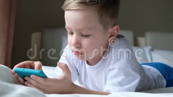 可爱的小男孩蹒跚学步玩手机游戏躺在床上拿着智能手机视频的预览图
