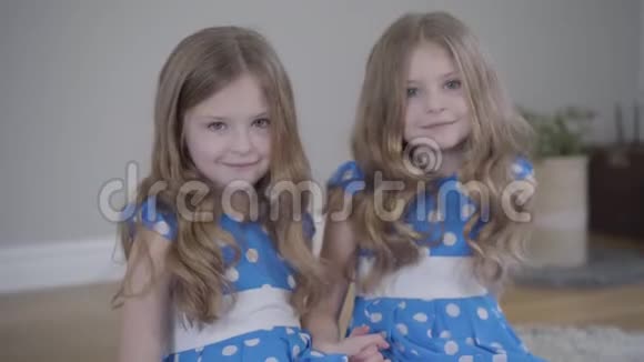 两个迷人的黑发小女孩看着镜头微笑的肖像穿着类似衣服的高加索双胞胎姐妹视频的预览图