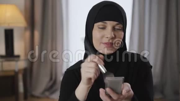 为美丽的穆斯林妇女敷脸粉穿着黑色头巾在家化妆的东部美女现代视频的预览图