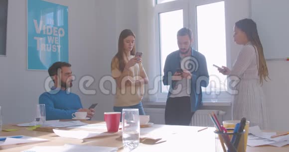 四位不同种族的同事在办公室喝咖啡休息时间使用智能手机现代互联网问题视频的预览图