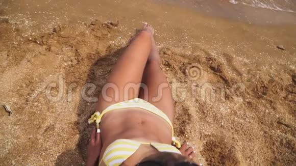 美丽的运动女孩穿着黄色泳衣躺在沙滩上在海边晒日光浴慢动作视频的预览图