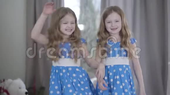 快乐的双胞胎姐妹在室内玩得很开心快乐的黑发白种人女孩穿着类似的蓝色点缀连衣裙视频的预览图