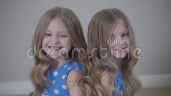 两个开朗的高加索双胞胎姐妹背靠背坐在一起谈笑风生的肖像类似的快乐孩子视频的预览图
