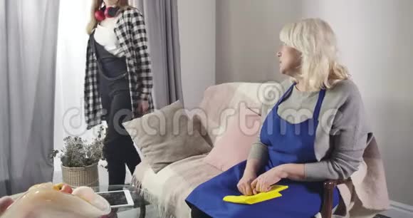 悲伤的白种人老妇人坐在蓝色围裙的沙发上十几岁的孙女走了过来让她平静下来勤奋视频的预览图