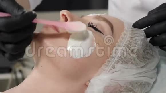 在美容院美容师在水疗沙龙里给女性脸皮戴上面具美容师使用升降霜视频的预览图