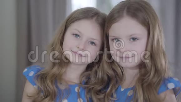 镜头从迷人的小双胞胎姐妹的脸上移开对着镜头微笑快乐友好女孩摆姿势的肖像视频的预览图