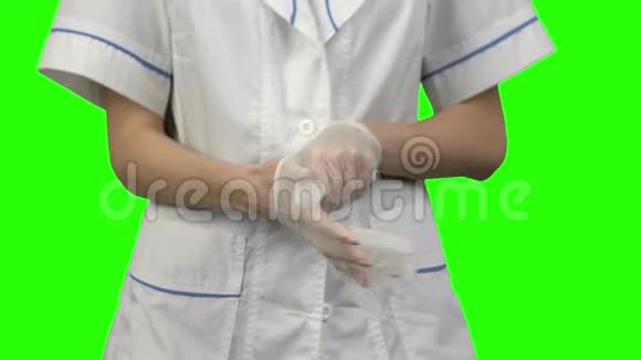 女人的双手戴上隔离在绿色背景上的乳胶手套视频的预览图