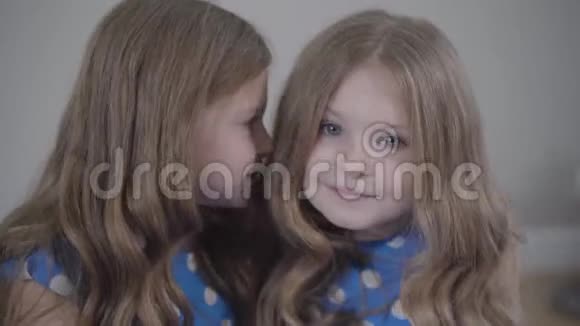 一个漂亮的白种人小女孩的特写镜头在双胞胎妹妹耳边低语并表现出安静的姿态快乐的双胞胎视频的预览图