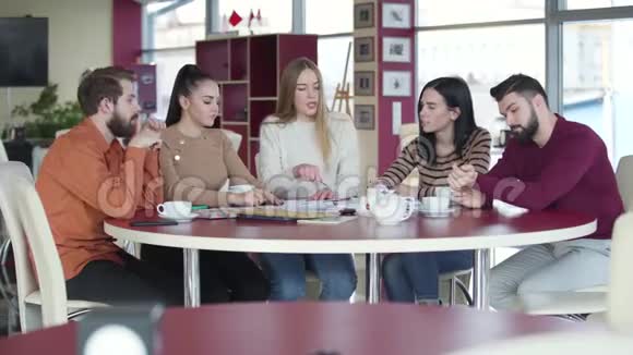 五个白人大学生在咖啡馆里讨论项目站起来离开年轻男女完成他们的视频的预览图