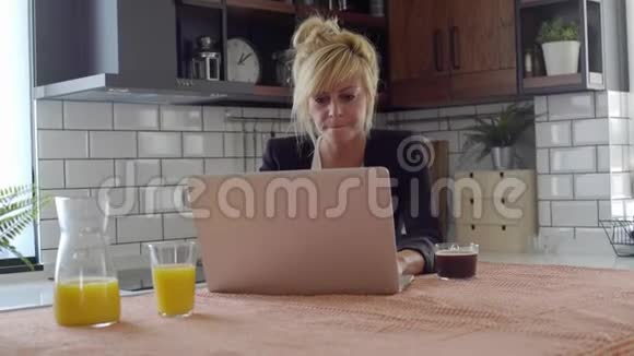 年轻的金发商务女性在厨房用笔记本电脑打字时感到沮丧视频的预览图