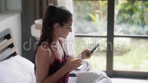 带果汁的女孩在大床上用智能手机上网视频的预览图