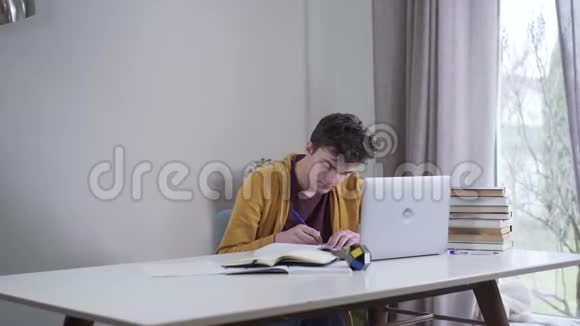 镜头靠近疲惫聪明的白人男孩他正在桌边写字妈妈端着茶和糖果走过来忧心忡忡视频的预览图