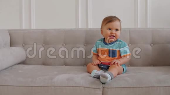 快乐的1岁男婴坐在沙发上对着镜头微笑视频的预览图