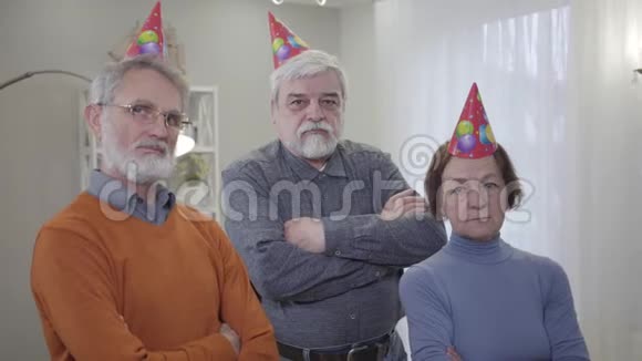 三个成熟的白人退休人员戴着派对帽看镜头的肖像在养老院摆姿势的长者视频的预览图