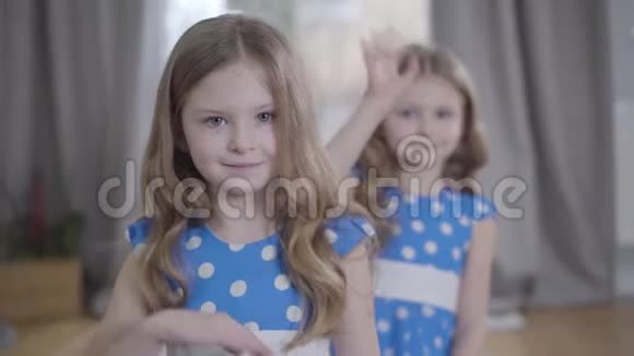 两个白人黑发双胞胎在镜头前挥手可爱的快乐姐妹穿着蓝色点缀的裙子享受免费视频的预览图