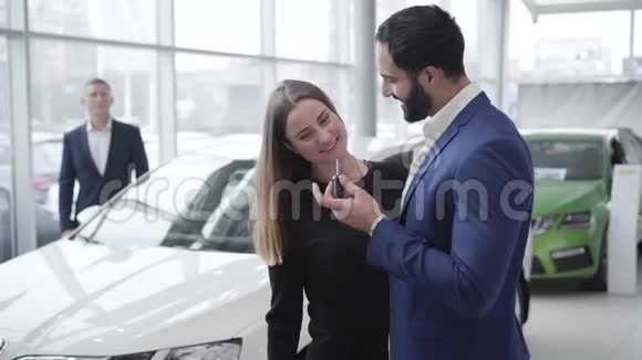 富有成功的中东男人在展厅给漂亮的高加索女人送车钥匙快乐的年轻夫妇视频的预览图