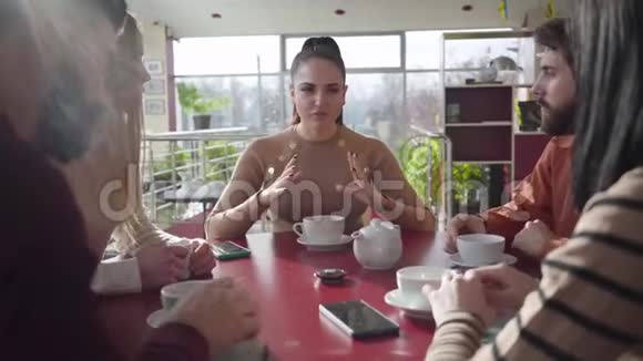 一群朋友坐在阳光明媚的日子里在咖啡馆里聊天自信的黑发白种人女人说话视频的预览图