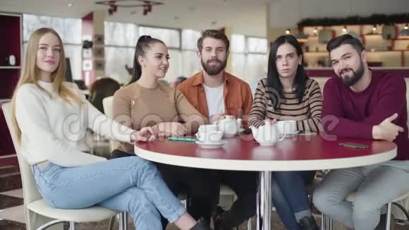 五个年轻的白种人坐在咖啡馆里看着摄像机微笑着友好的伙伴摆姿势视频的预览图