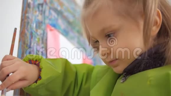 一个小女孩在一个艺术工作室里坐在画架上画画视频的预览图