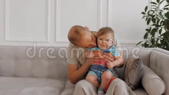 快乐的孩子坐在爸爸的腿上笑爸爸抱着小儿子亲吻他视频的预览图
