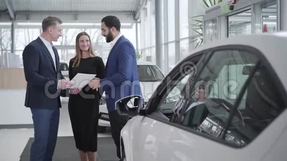 年轻富有的多种族家庭在经销商购买汽车微笑中东客户和高加索经销商握手视频的预览图