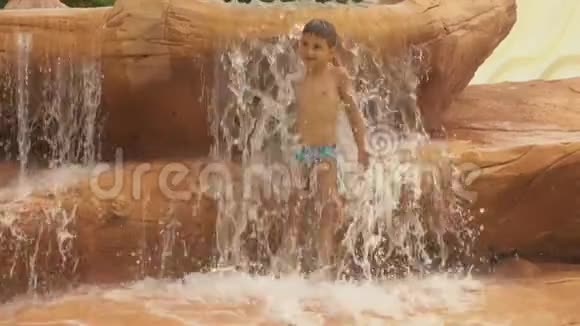 小男孩站在水上乐园的瀑布下视频的预览图