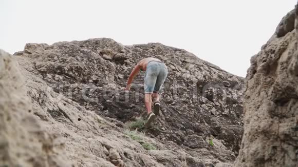 运动员赤裸着上身爬上岩石慢动作下角度视频的预览图