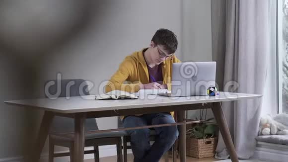 长镜头聪明的白种人男孩戴着眼镜看着笔记本电脑屏幕和写作自信的青少年学生视频的预览图