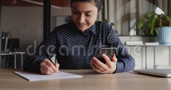 微笑着拿着智能手机的年轻印度女学生工人做笔记视频的预览图