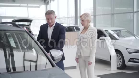 汽车经销商为成功的成年高加索女商人在展厅打开车门富有的女性客户选择视频的预览图