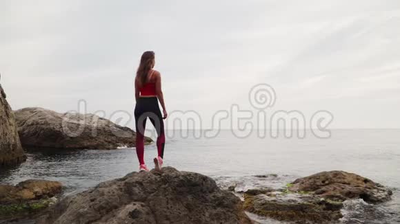 在海中的一块石头上是一件运动的女孩旅行运动服慢动作视频的预览图