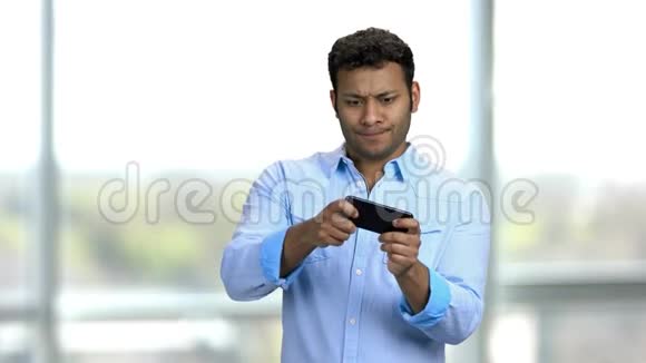 年轻热情的印度男人在他的智能手机上玩电子游戏视频的预览图